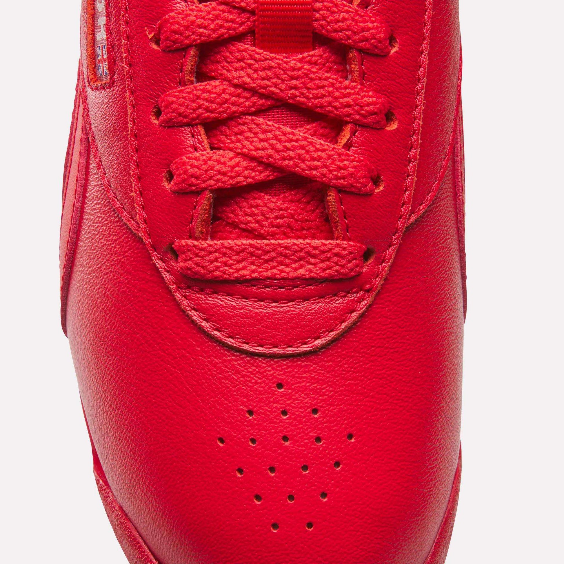 Close-up of the toe and laces of a red Reebok Women's Freestyle Lo Shoe, featuring a leather finish, red laces, toe perforations, and part of a fabric label on the side.