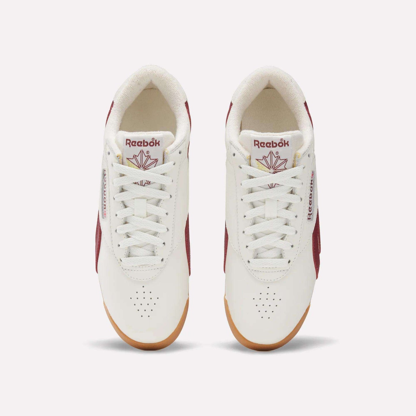 Top view of Women's Freestyle Lo Shoes by Reebok in white with maroon accents, gum soles, and logo with red maple leaf on the tongue. These women's retro sneakers are neatly laced and set side by side on a light background.