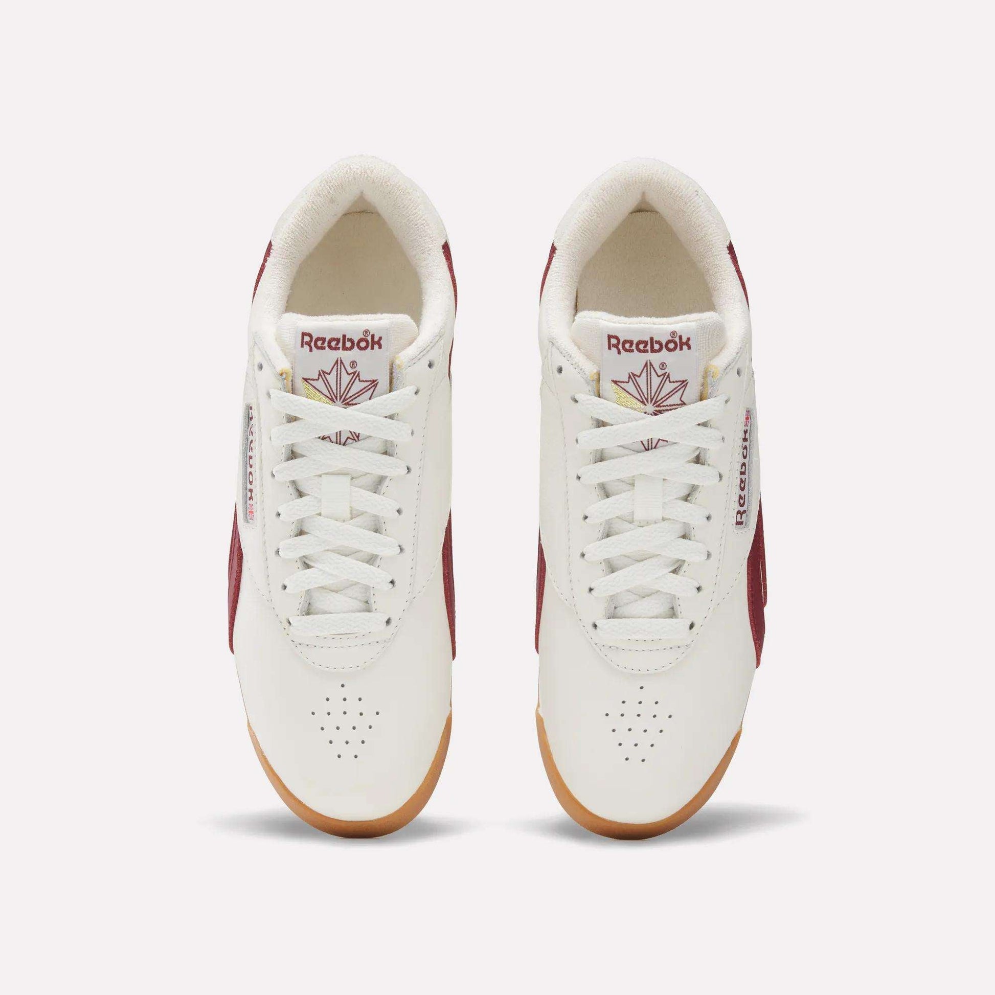 Top view of Women's Freestyle Lo Shoes by Reebok in white with maroon accents, gum soles, and logo with red maple leaf on the tongue. These women's retro sneakers are neatly laced and set side by side on a light background.