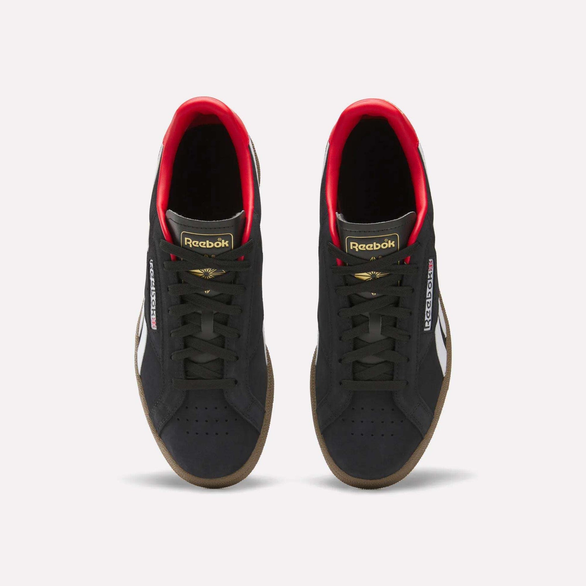 A pair of Reebok Club C Grounds UK Shoes in black with white side stripes, gold and red accents, black laces, and gum soles are shown from above on a white background—a perfect classic tennis-style casual shoe.