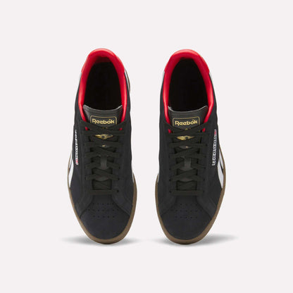 A pair of Reebok Club C Grounds UK Shoes in black with white side stripes, gold and red accents, black laces, and gum soles are shown from above on a white background—a perfect classic tennis-style casual shoe.