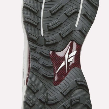 Close-up of Reebok Nano Golf Shoes sole featuring a rugged grey tread, red and black carbon fiber midsection, and white logo—designed for performance with a lightweight FlexWeave upper for optimal comfort.