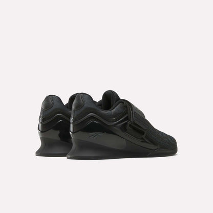 The Reebok Women's Legacy Lifter IV Training Shoes feature elevated heels, mesh uppers, wide straps, and glossy accents, shown from the back and side on a plain white background for support and stability.