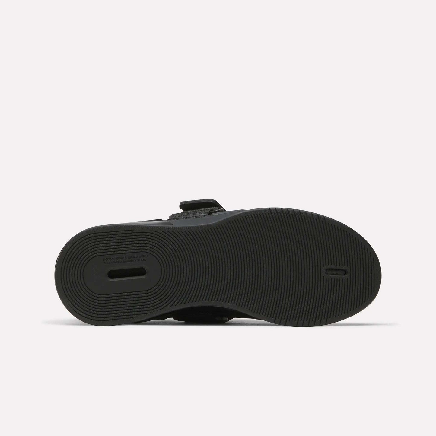 The image displays the black rubber sole of Reebok Women's Legacy Lifter IV Training Shoes, with a textured circular tread and a rectangular heel cut-out for support. The shoe is shown sole-up on a plain white background.