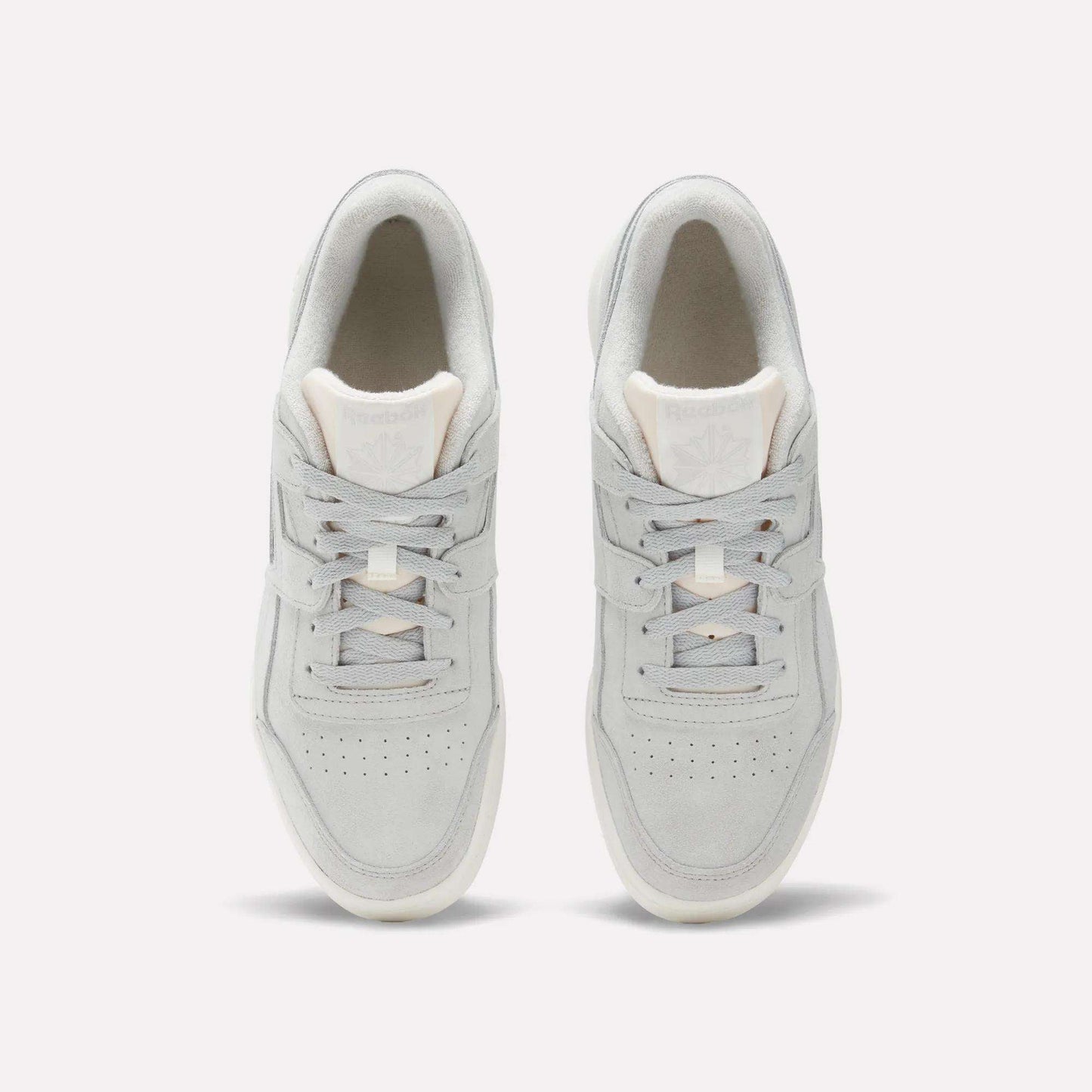 Top view of Reebok Workout Plus Shoes in light gray with white soles, laces, and subtle branding on the tongue. These classic sneakers channel authentic '80s fitness style and are shown side by side on a plain white background.