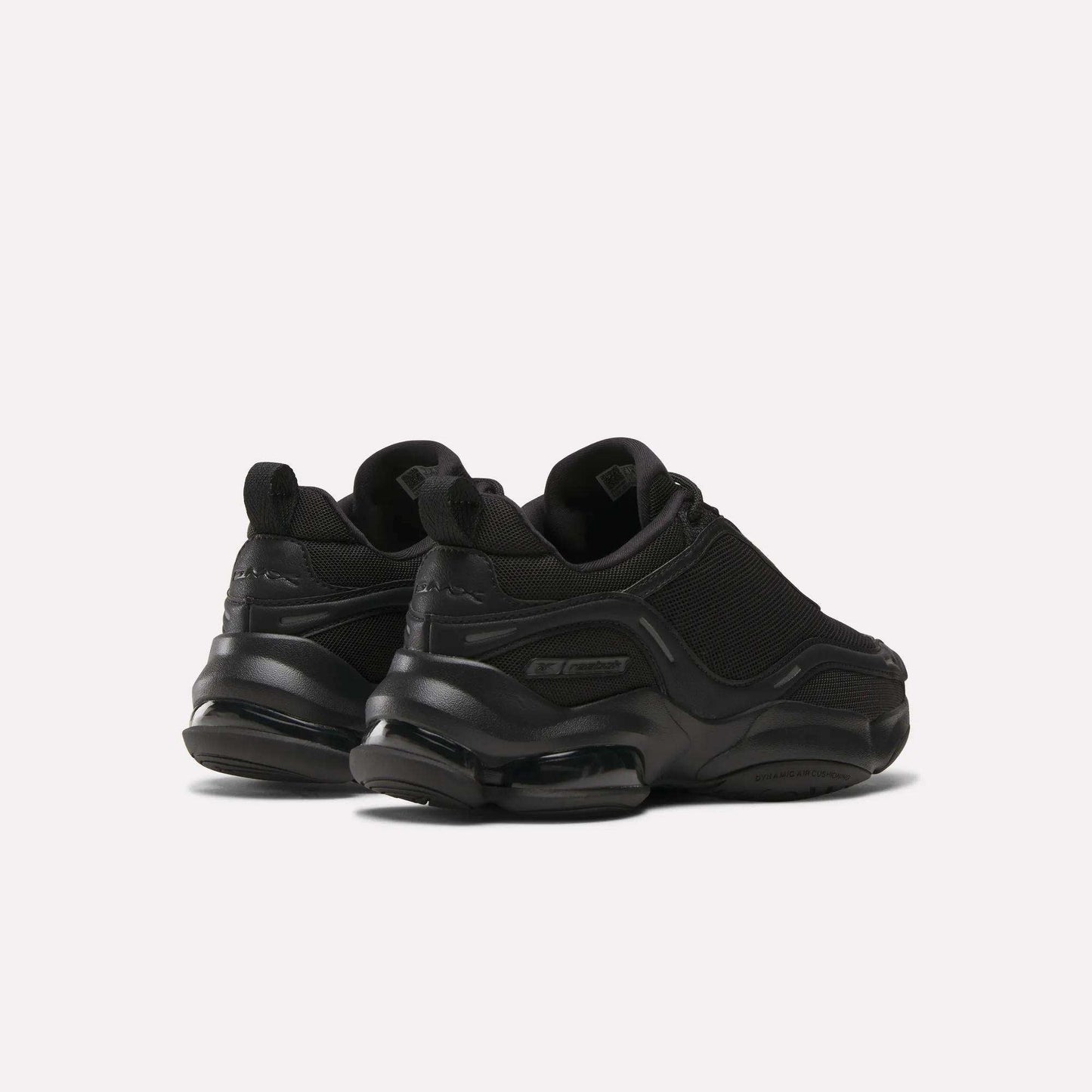 A pair of Reebok Women's DMX Series 3000 Training Shoes in black, with chunky soles, DMX 3 Technology, mesh and synthetic uppers, and subtle branding, shown on a plain light background from the back and side angles.
