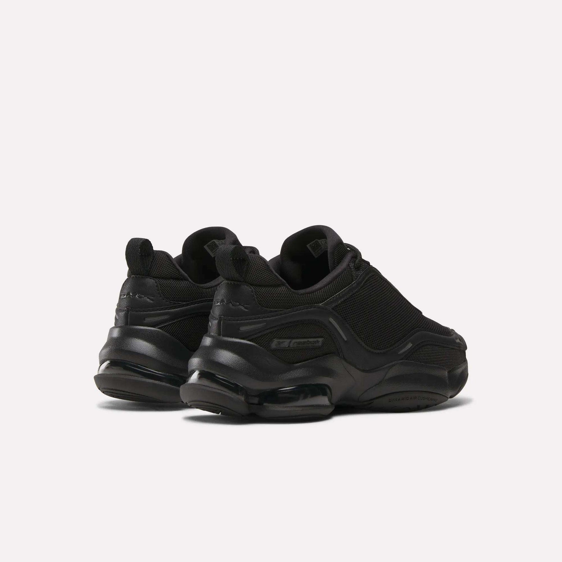 A pair of Reebok Women's DMX Series 3000 Training Shoes in black, with chunky soles, DMX 3 Technology, mesh and synthetic uppers, and subtle branding, shown on a plain light background from the back and side angles.