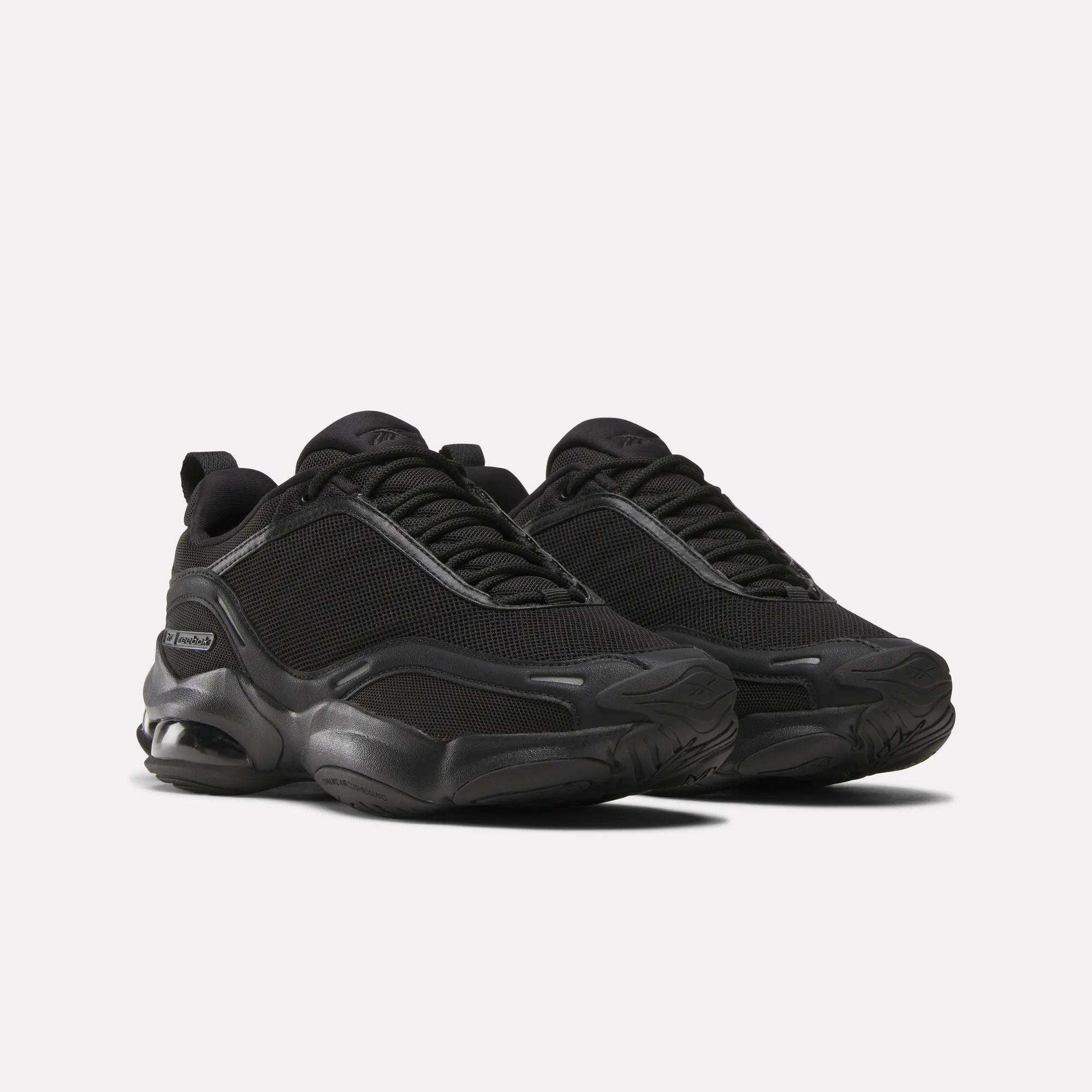 A pair of Women's DMX Series 3000 Training Shoes by Reebok in black, featuring mesh uppers, DMX 3 Technology thick textured soles, and black laces, displayed on a light background.