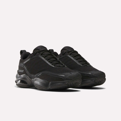 A pair of Women's DMX Series 3000 Training Shoes by Reebok in black, featuring mesh uppers, DMX 3 Technology thick textured soles, and black laces, displayed on a light background.