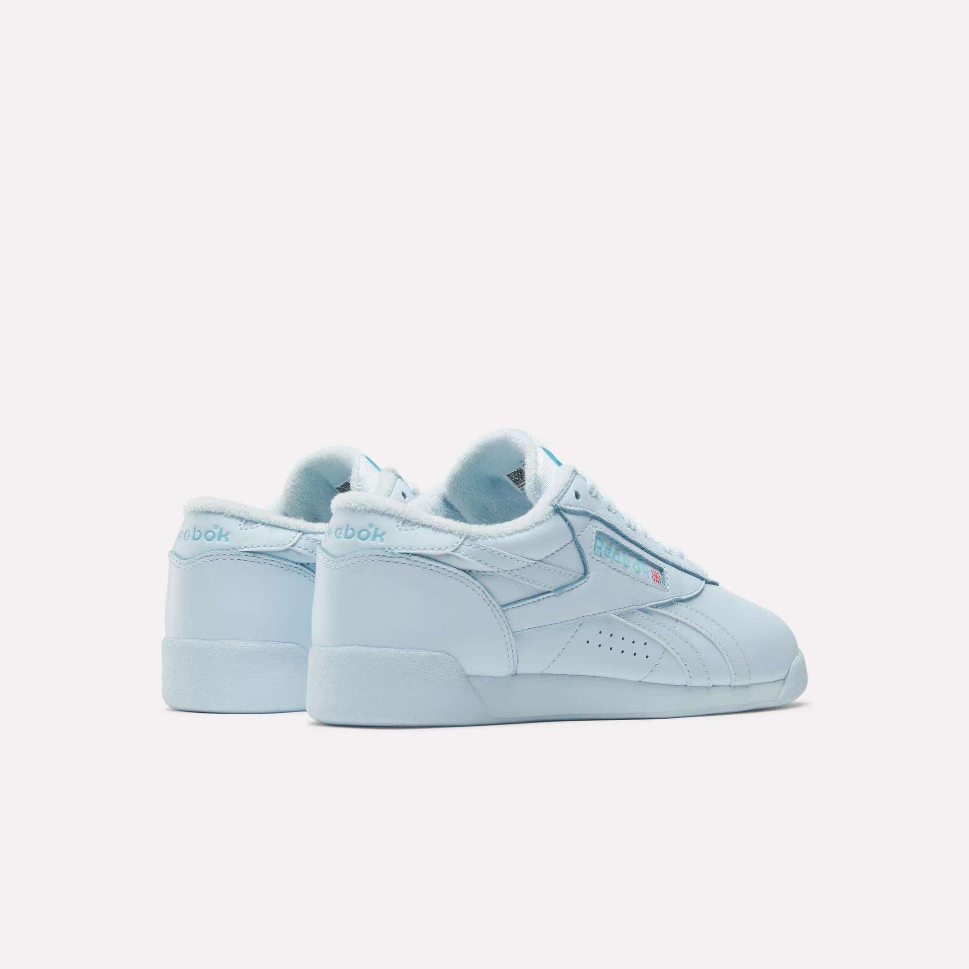 A pair of light blue Reebok Women's Freestyle Lo Shoes are shown on a white background—one facing forward, the other angled to reveal the iconic Reebok logo and branding—ideal for everyday wear.