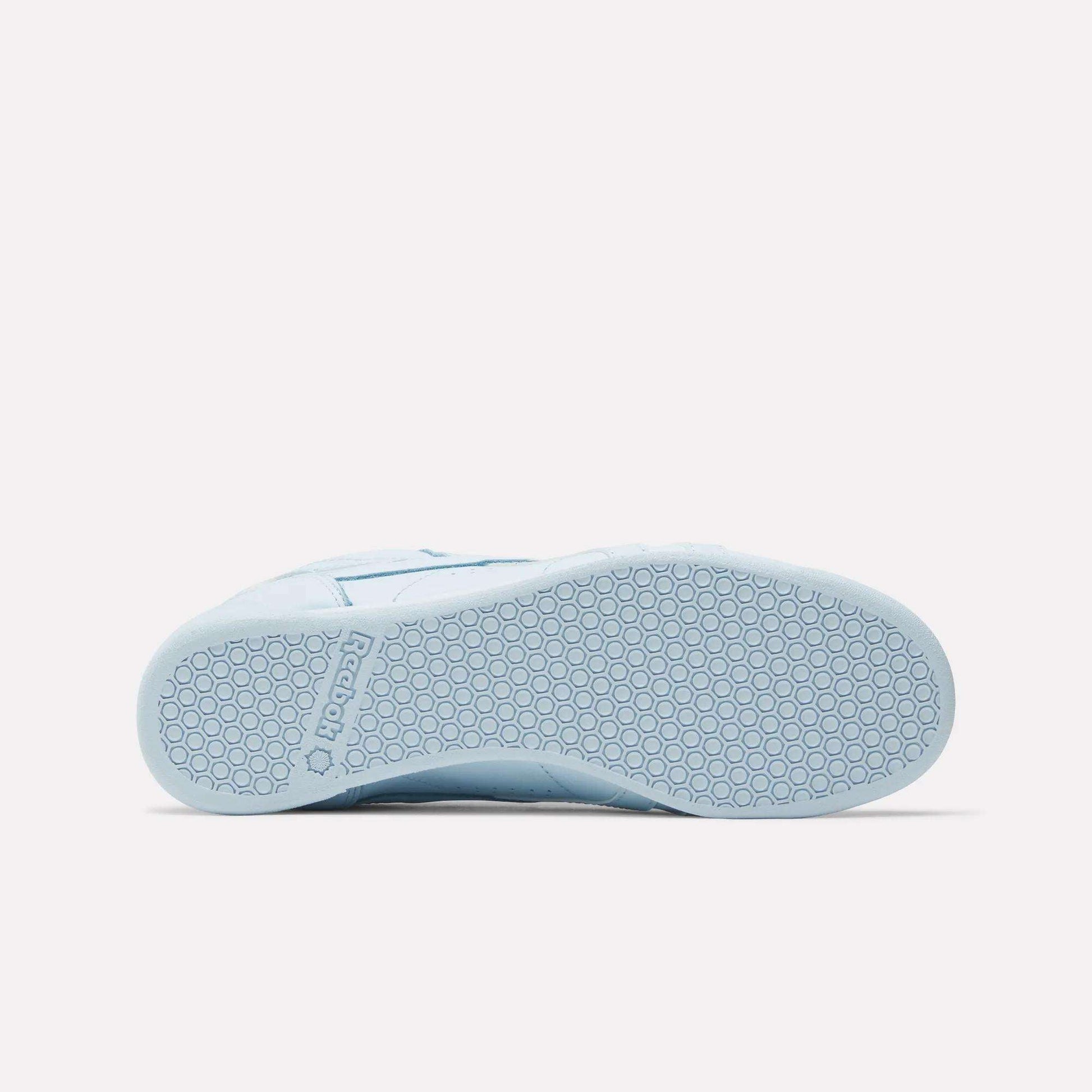 The Women's Freestyle Lo Shoes by Reebok in light blue are shown from the bottom, featuring a textured rubber sole with a hexagonal pattern and the Reebok logo embossed near the heel—ideal for everyday wear.