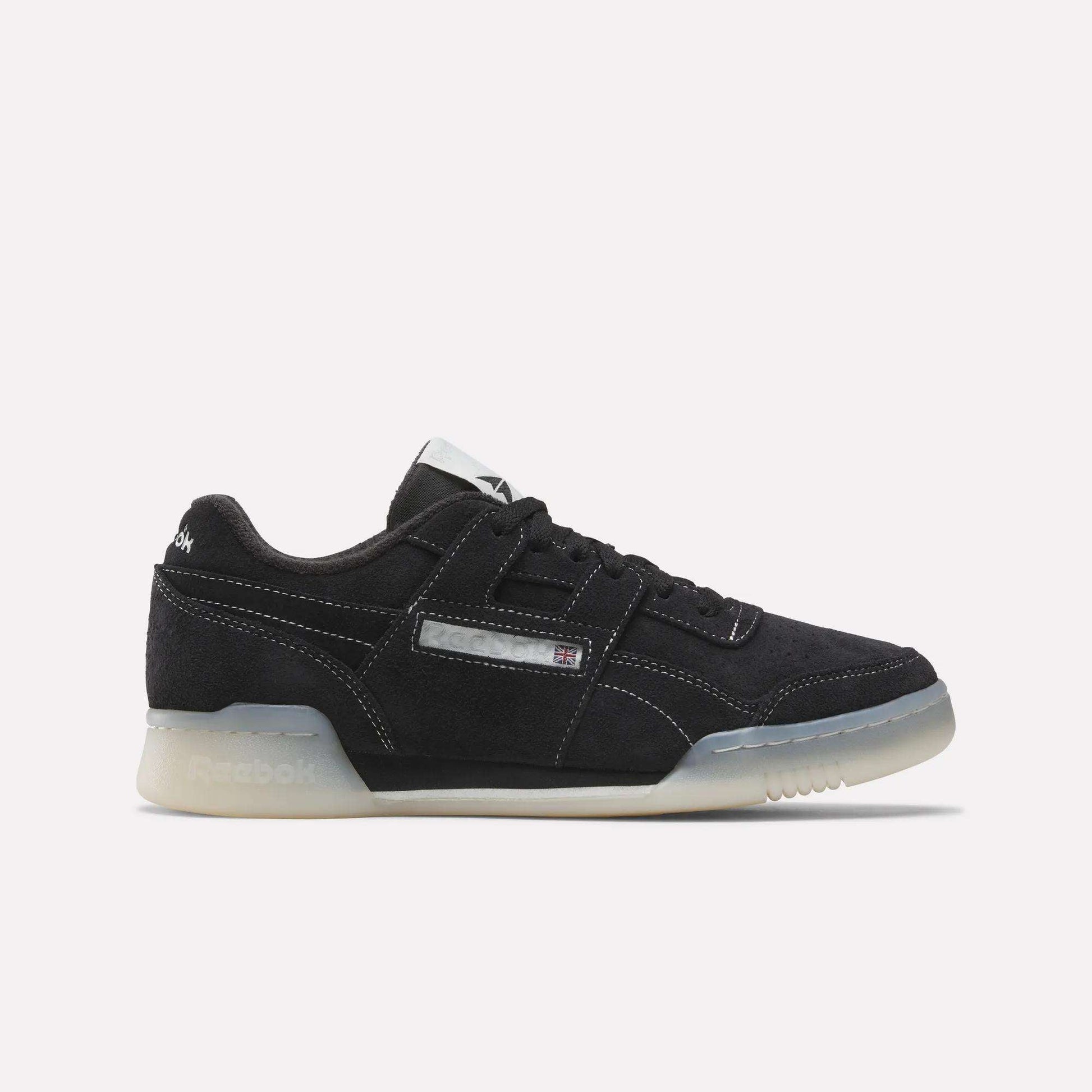 The Reebok Workout Plus Shoes feature a black design with white stitching, translucent off-white sole, and a small Union Jack logo on the side, capturing classic '80s fitness style against a plain white background.
