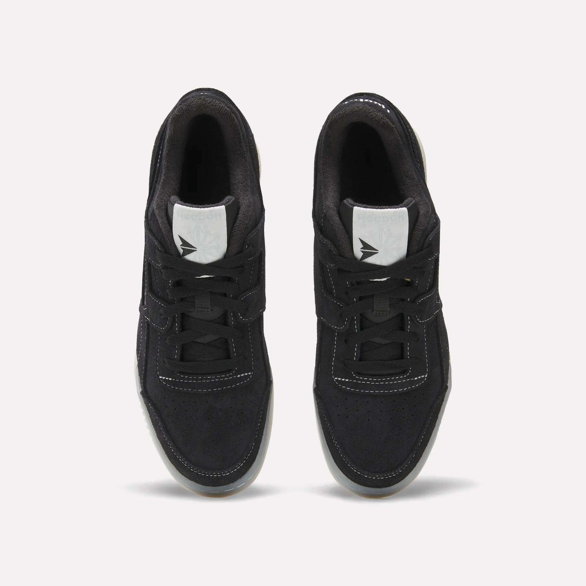 A pair of Reebok Workout Plus Shoes in black with white stitching and tongue labels, seen from above on a light background. The tied laces and side-by-side placement highlight their classic '80s-inspired fitness style.