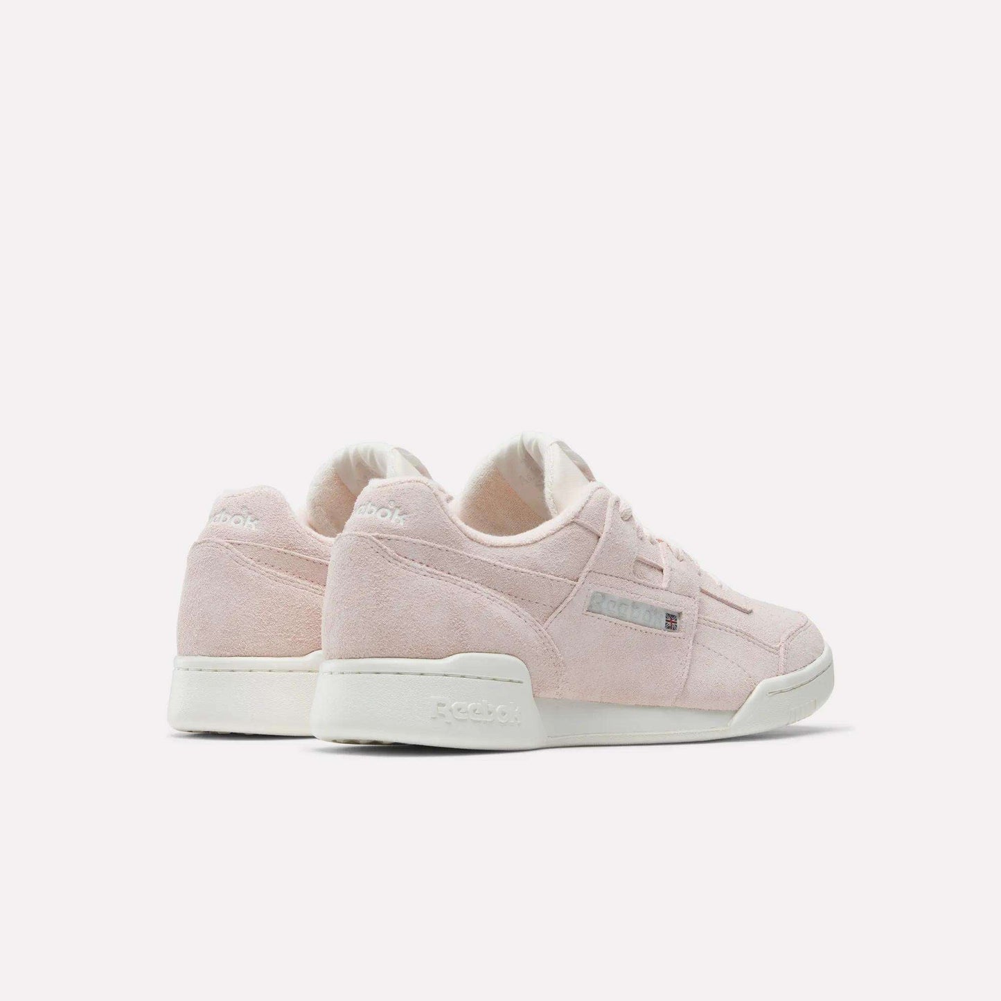 A pair of Reebok Workout Plus Shoes in light pink suede with white soles, displayed on a plain white background and angled to showcase the side and back views, highlighting their iconic '80s fitness style.