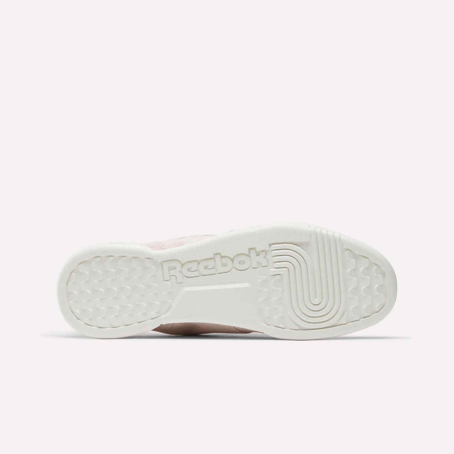 The image shows the bottom sole of Reebok Workout Plus Shoes with the Reebok logo embossed in the center and textured grip patterns, all in an off-white color inspired by classic '80s fitness style.