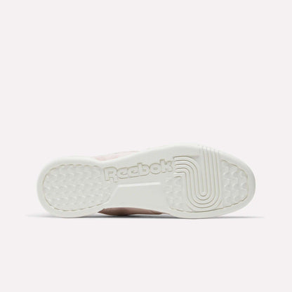 The image shows the bottom sole of Reebok Workout Plus Shoes with the Reebok logo embossed in the center and textured grip patterns, all in an off-white color inspired by classic '80s fitness style.
