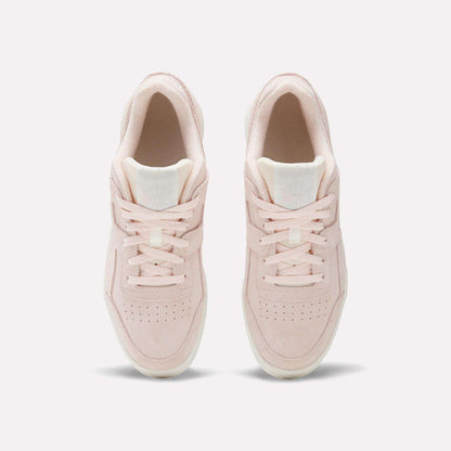 The Reebok Workout Plus Shoes are shown from above on a white background, featuring light pink suede, laces, and toe box perforations that blend classic ’80s fitness style with modern comfort.