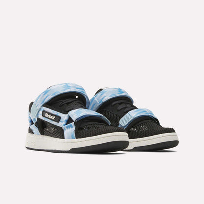 The Reebok x MARKET Club C 85 Shoes feature black mesh uppers, thick white soles, blue and white tie-dye Velcro straps, and “Market” branding—a bold collaboration blending tennis-inspired style.