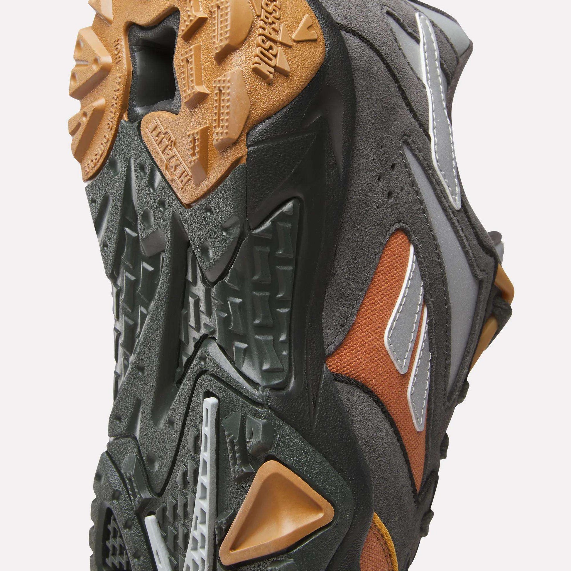 Close-up of the Reebok x MARKET Preseason 94 Low Shoes, featuring a rugged dark green, brown, and gum sole. Reflective and orange accents on the upper make these Reebok trainers ideal for any preseason collection.