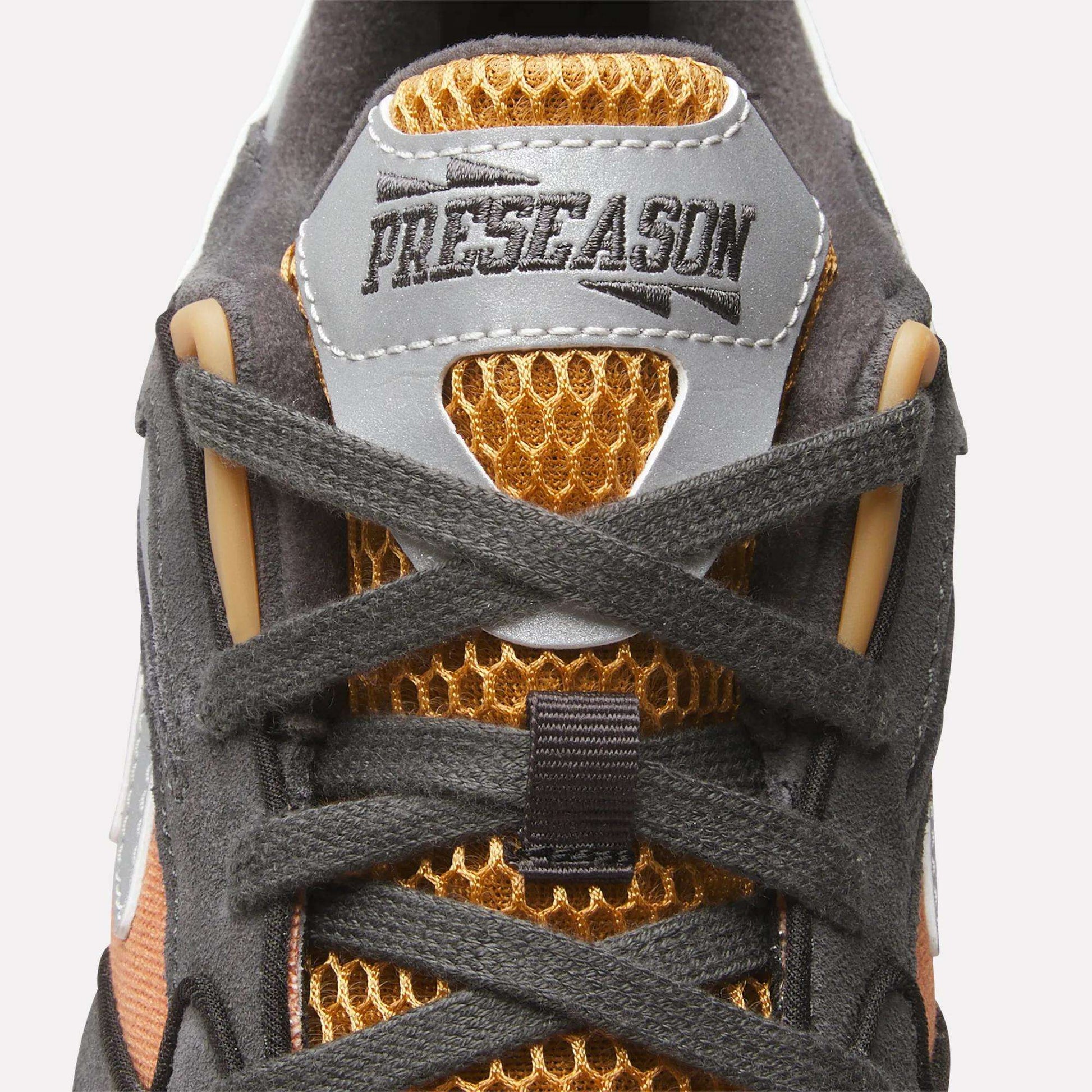 Close-up of the Reebok x MARKET Preseason 94 Low Shoes sneaker’s tongue shows honeycomb-textured orange mesh, gray laces, and a “PRESEASON” patch. Dynamic black and gold details highlight this Reebok design from the Preseason collection.
