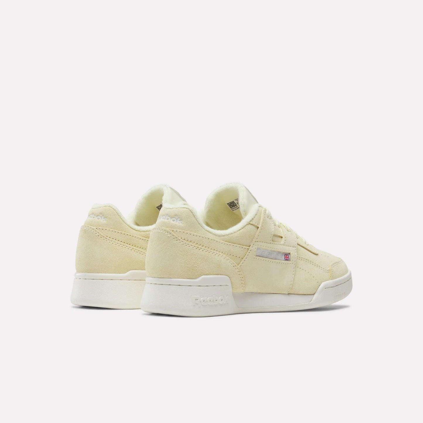 A pair of Women's Workout Plus Shoes by Reebok in light yellow suede with white soles, shown from the back and side on a white background. Classic '80s fitness style and subtle branding complete these women's sneakers.