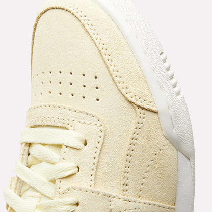 Close-up of the upper front of the Reebok Women's Workout Plus Shoes, featuring beige suede, double perforations, cream laces, and a white textured rubber sole—a classic '80s-inspired fitness style.