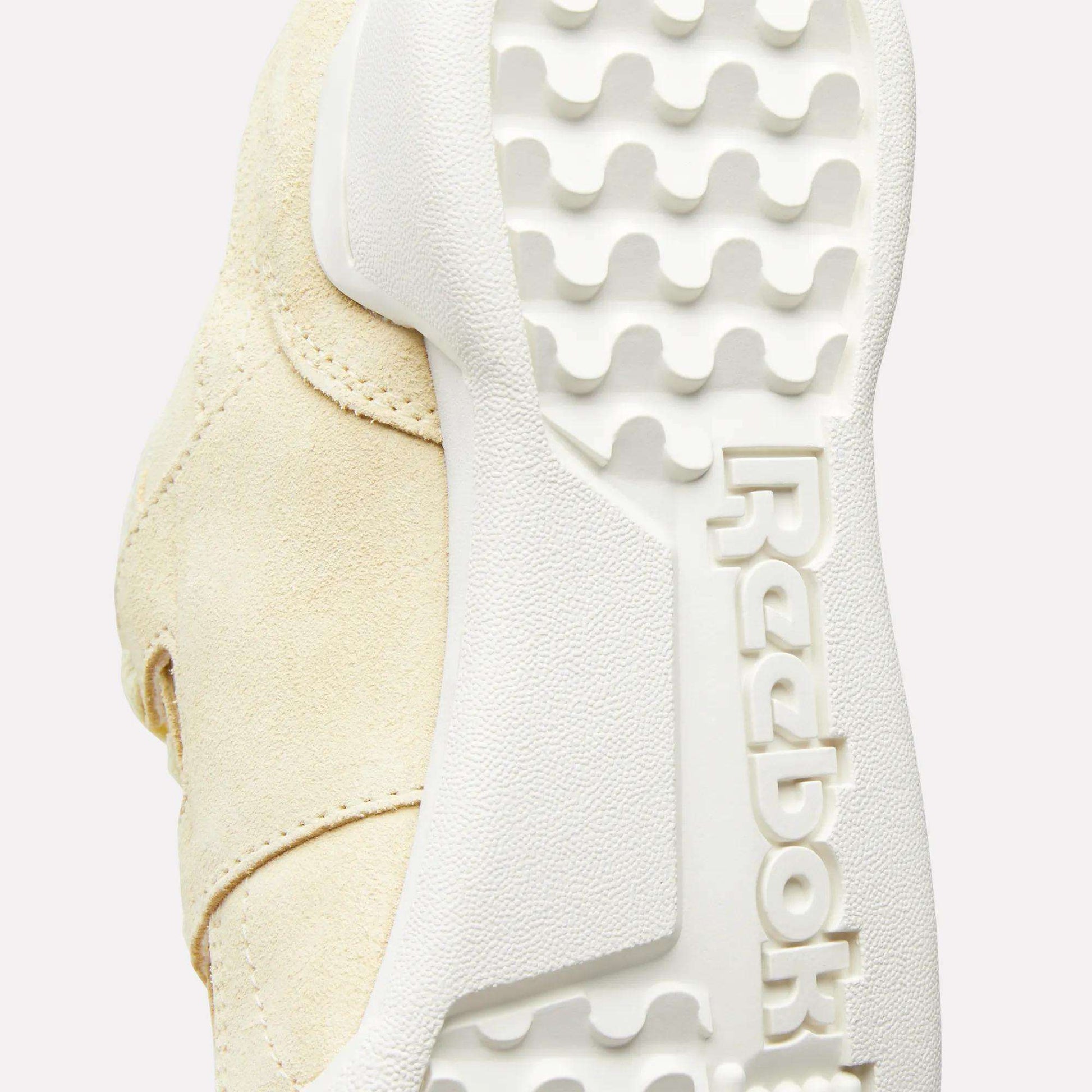 Close-up of the sole of the Women's Workout Plus Shoes by Reebok, highlighting the textured white rubber outsole with an embossed Reebok logo and a wavy tread pattern inspired by '80s fitness style.