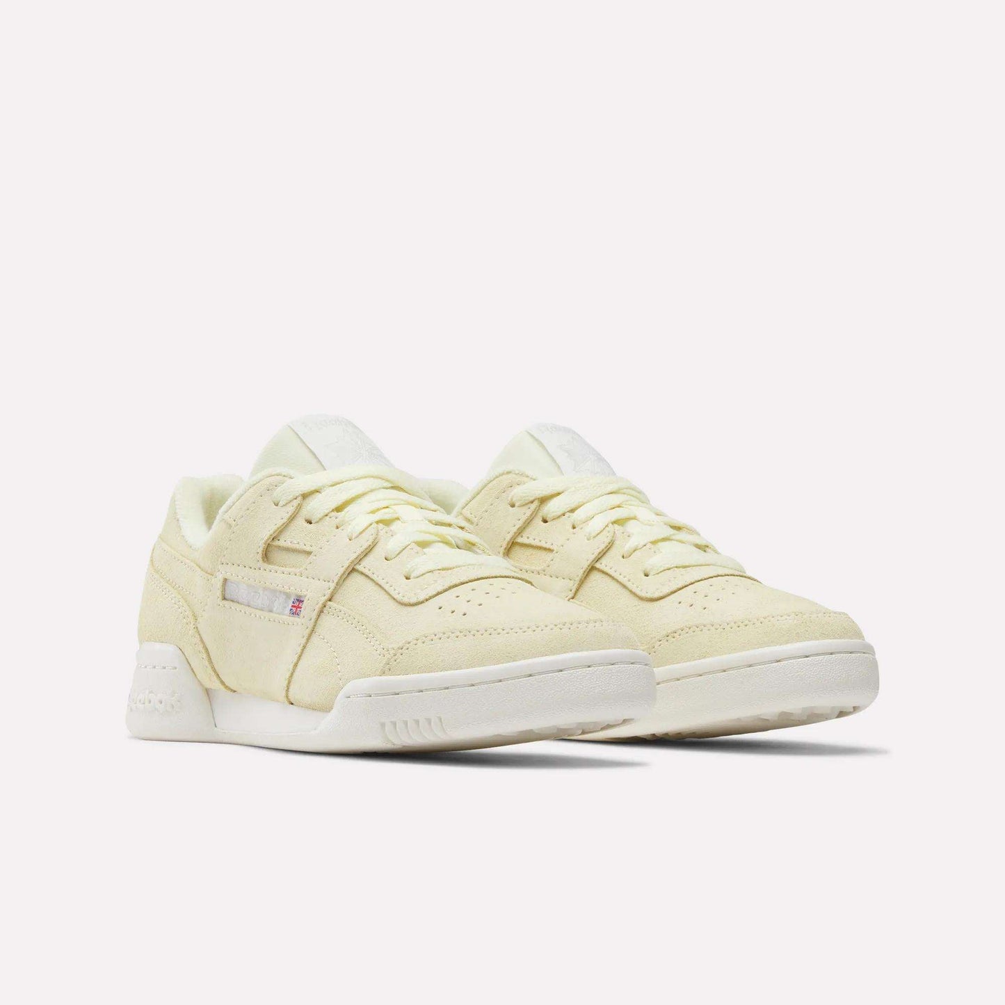 A pair of Women's Workout Plus Shoes by Reebok in pale yellow with white soles, lace-up fronts, and subtle side branding capture classic '80s fitness style, shown on a plain white background.