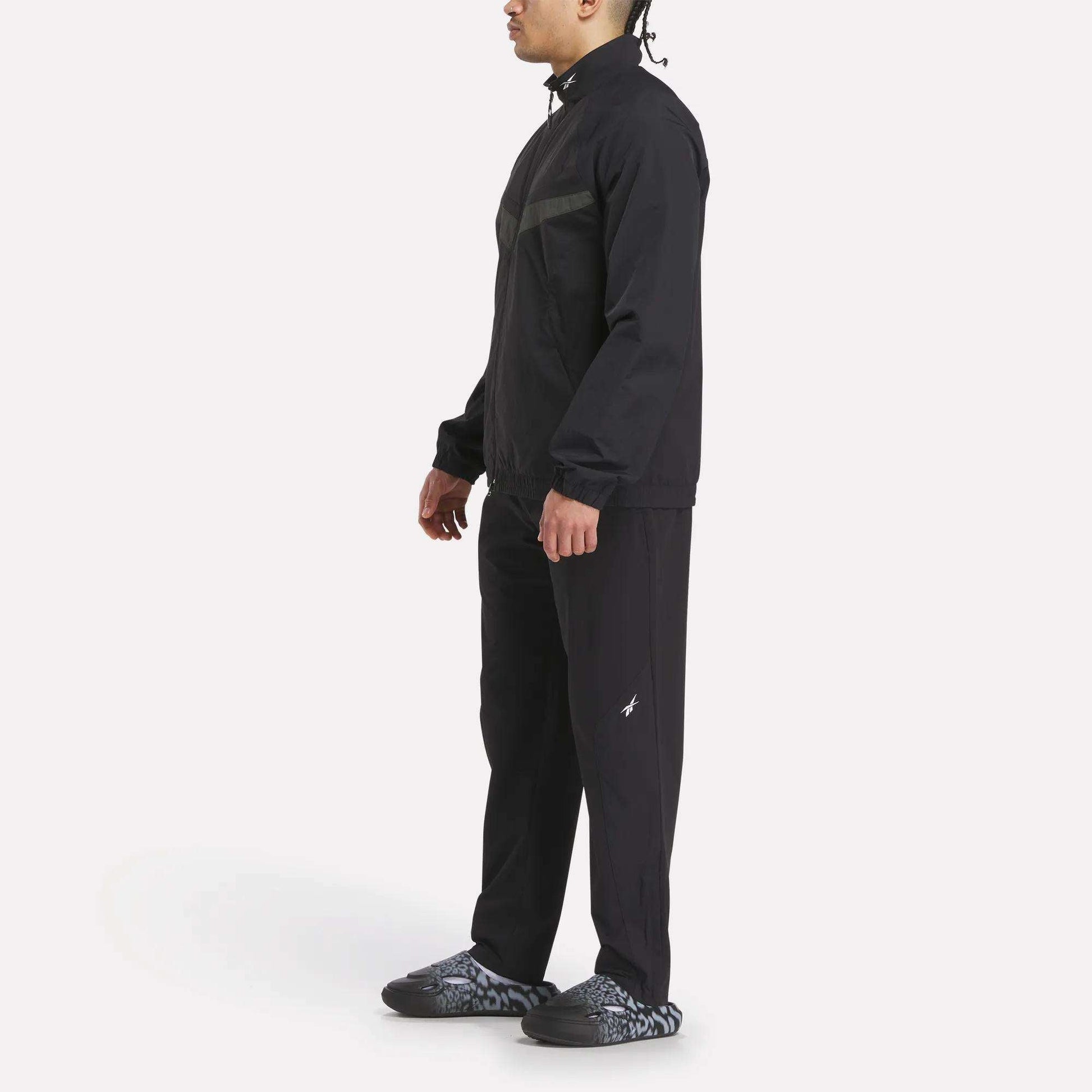 A person in profile wears a Reebok Warm Up Track Jacket and matching pants with light-patterned sneakers against a plain white background.