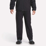 A person is shown from shoulders down wearing Reebok Track Pants, a black jacket, and black shoes against a plain white background.