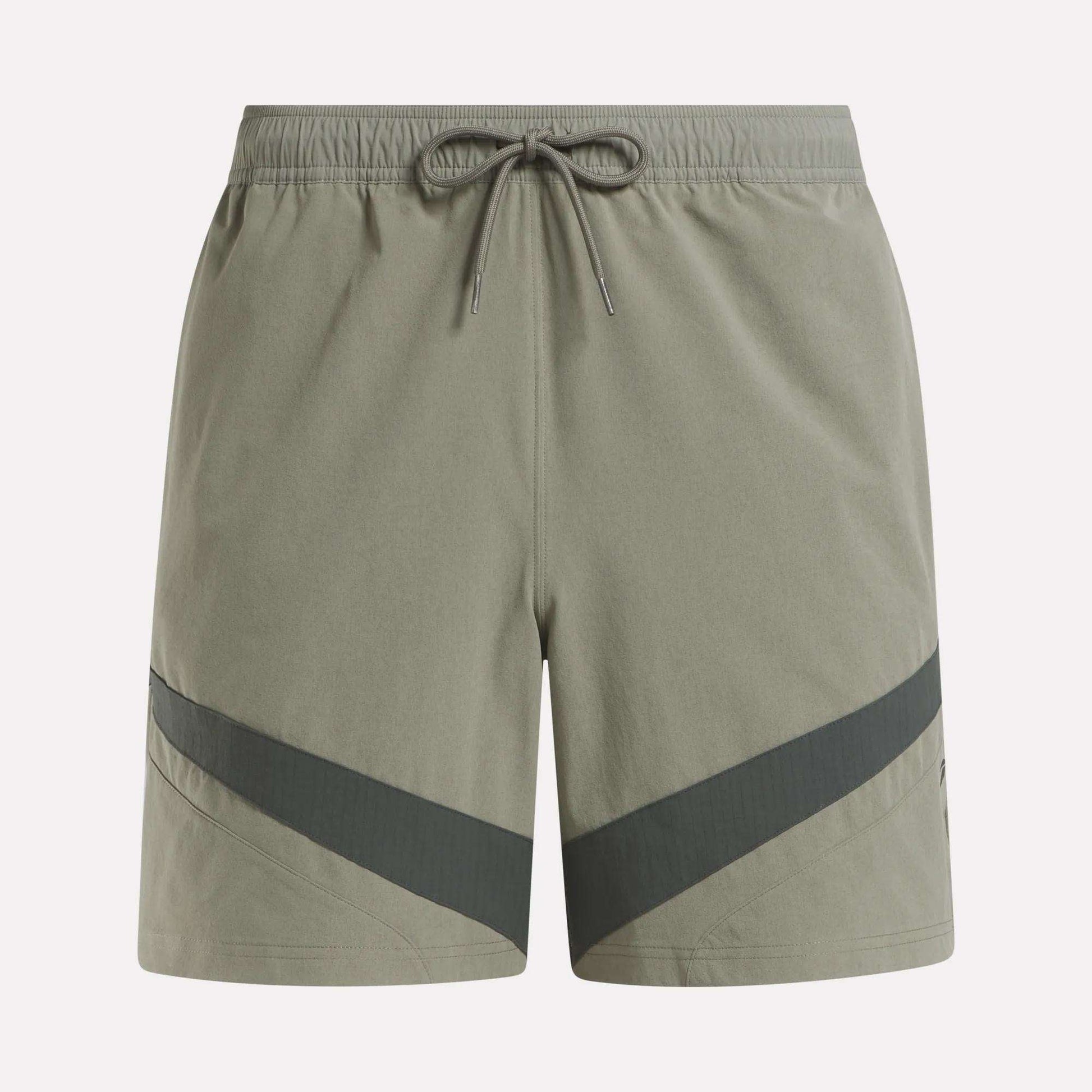 Reebok Woven Basketball Shorts in light olive green feature an elastic waistband with drawstring, dark diagonal stripes near the hem, and smooth, lightweight fabric—perfect for active wear or basketball enthusiasts.