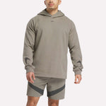 A man wears a light brown Reebok French Terry Basketball Hoodie with a small chest logo and matching shorts with dark diagonal stripes, standing against a plain white background.