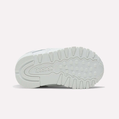 The image shows the sole of Reebok Kids' Classic Leather Shoes in white, featuring textured tread patterns and a central Reebok logo. These casual sneakers are perfect for everyday wear and are photographed against a plain, light-colored background.
