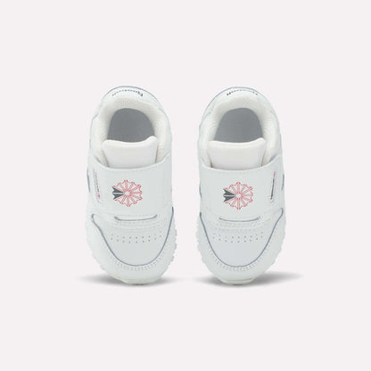 Kids' Classic Leather Shoes by Reebok for babies feature white leather, Velcro straps, a pink geometric star design, and small front text—ideal for everyday wear and shown on a plain light background.