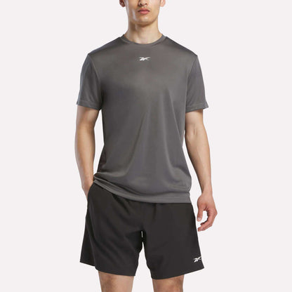 A person wears a Reebok Men's Short Sleeve Tech Training T-Shirt, featuring sweat-wicking fabric, and black shorts with small white logos, standing against a plain white background.