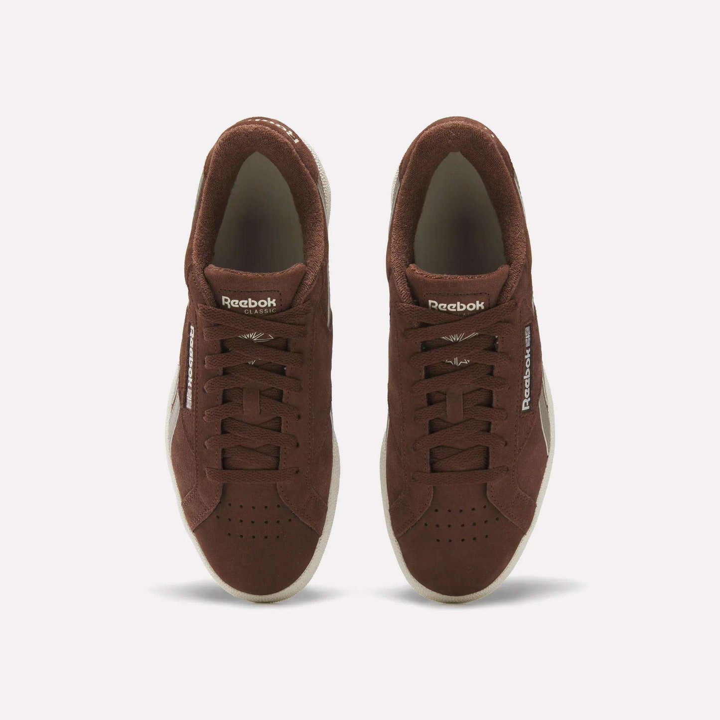 A pair of Reebok Club C Grounds UK Shoes in brown suede viewed from above, with white soles, laces, and Reebok branding on the tongue and side, delivering a classic vintage tennis style.