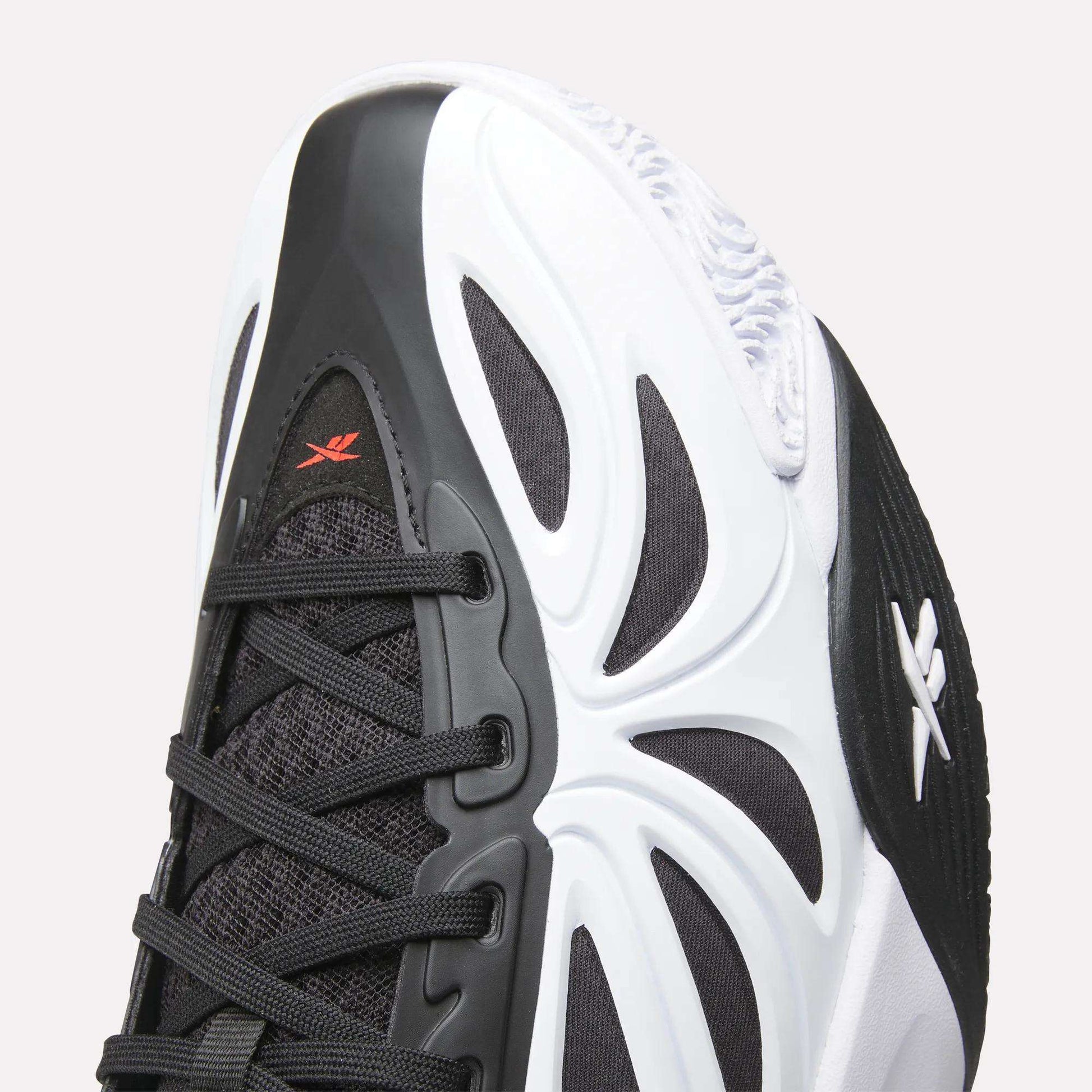 Close-up of the Reebok Angel Reese 1 Basketball Shoes—black and white design with black laces, white outsole, red logo near the toe, wavy patterns, and Energy Return System for peak basketball performance.