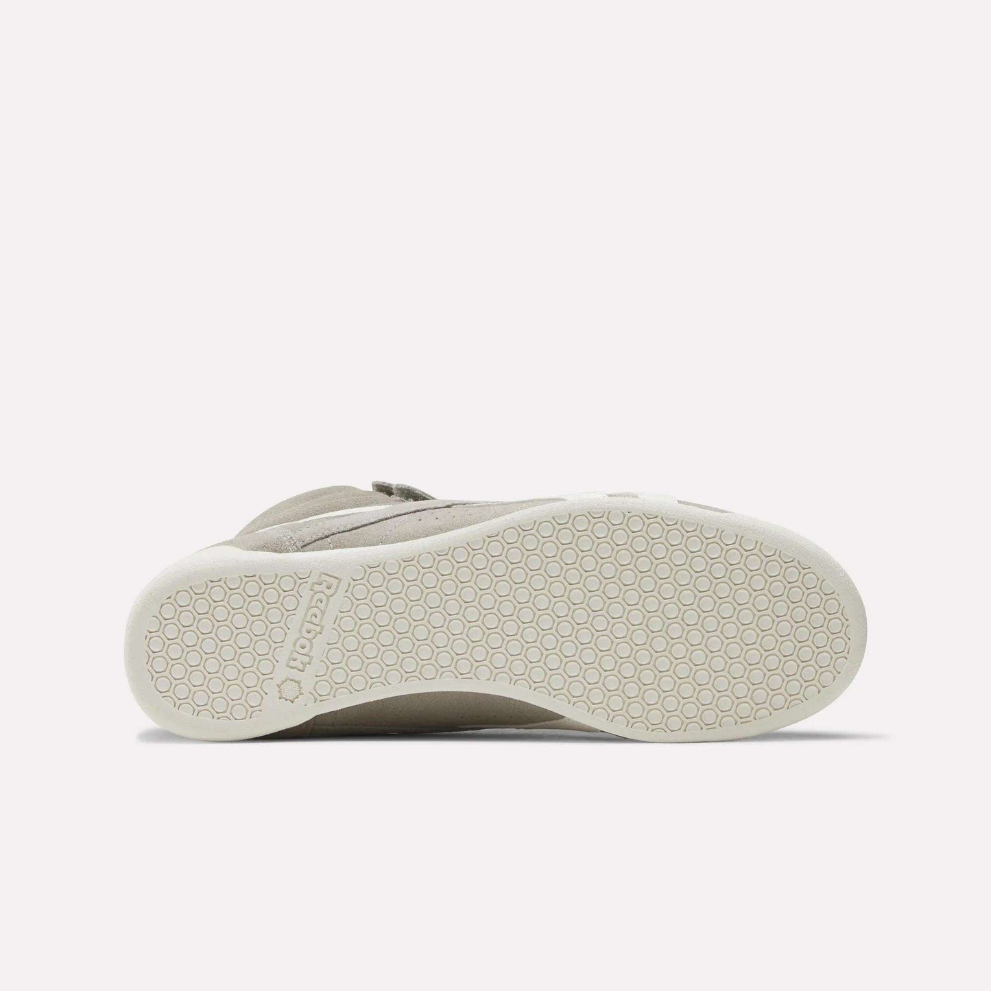 The image shows the bottom view of a beige Women's F/S Hi Shoe by Reebok, with a white sole featuring a hexagonal pattern and the Reebok name embossed near the heel, reflecting popular high top sneaker design trends.