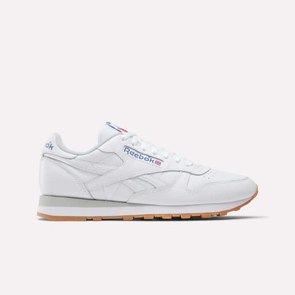 The Reebok Classic Leather Shoes are shown in white with a gum sole, blue and red Reebok side logo, and white laces, displayed in a retro-inspired side profile against a plain light background.