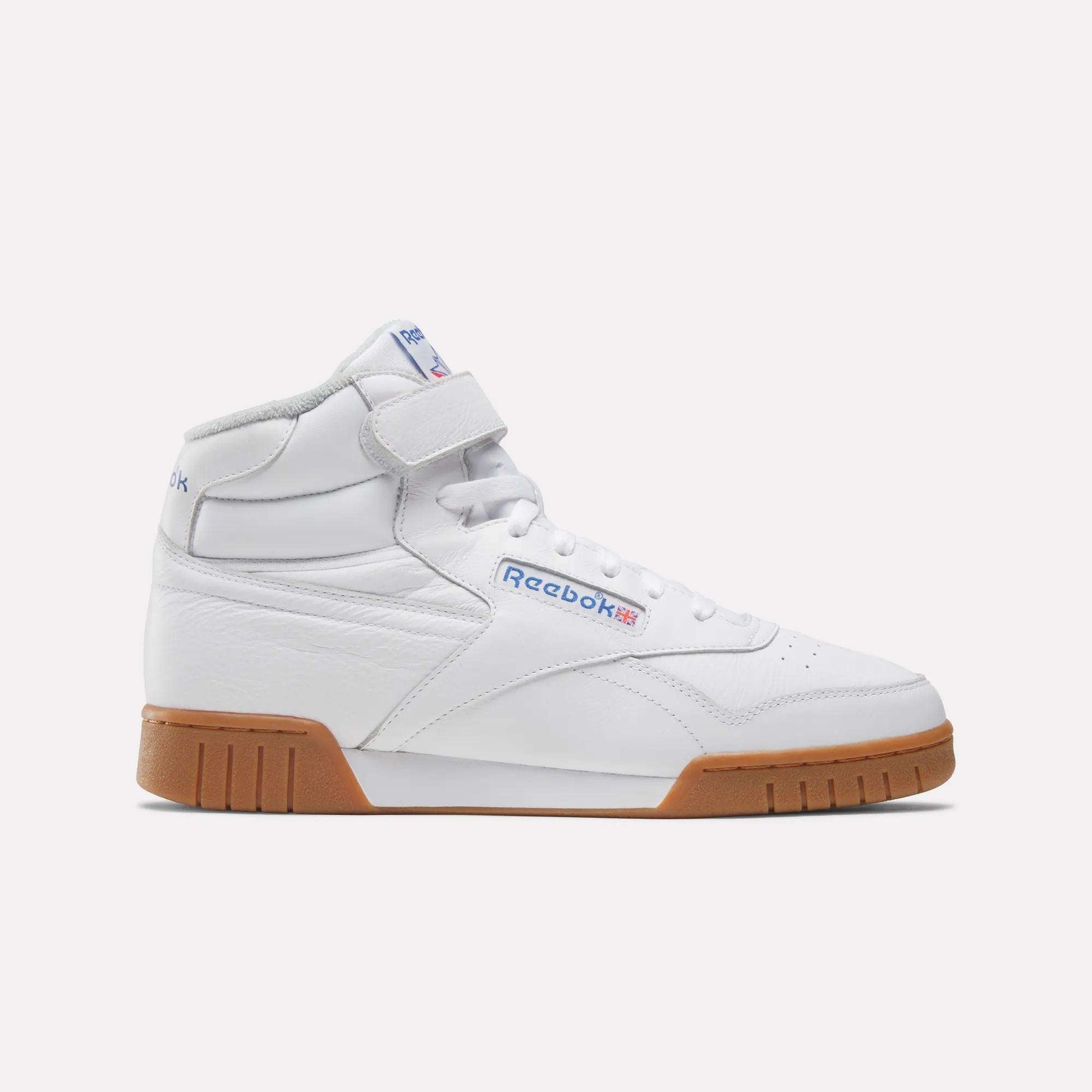 The Men's EX-O-FIT Hi Shoes by Reebok are white leather high-tops with a Velcro strap, blue and red Reebok branding, and a brown rubber sole, shown in side profile on a plain light background for a retro look.