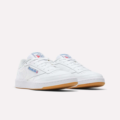 A pair of Reebok Men's Club C 85 Shoes in white leather with gum soles, featuring the Reebok logo and Union Jack on the side and tongue, displayed against a plain light background.
