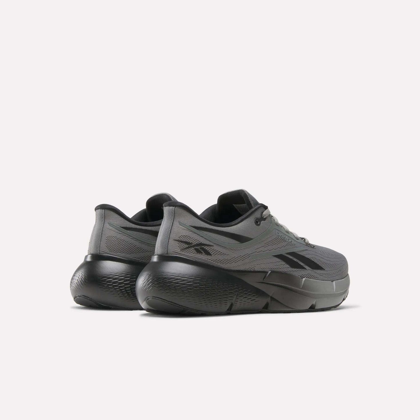 A pair of Reebok Men's Zignition Running Shoes in gray, featuring thick sculpted black soles, shown from a rear and side angle against a plain light background.