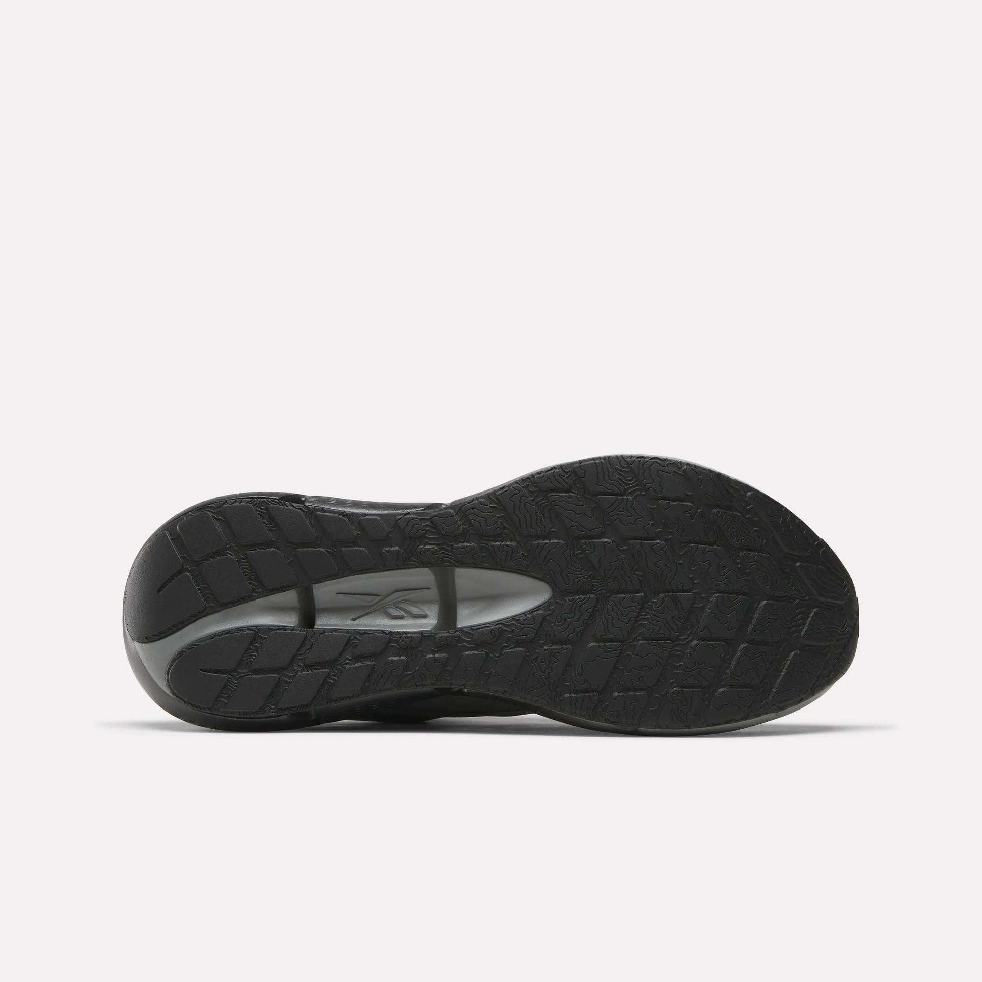 The image displays the black rubber sole of Reebok Men's Zignition Running Shoes, featuring a textured tread and visible brand logo at the midfoot, set against a plain white background.