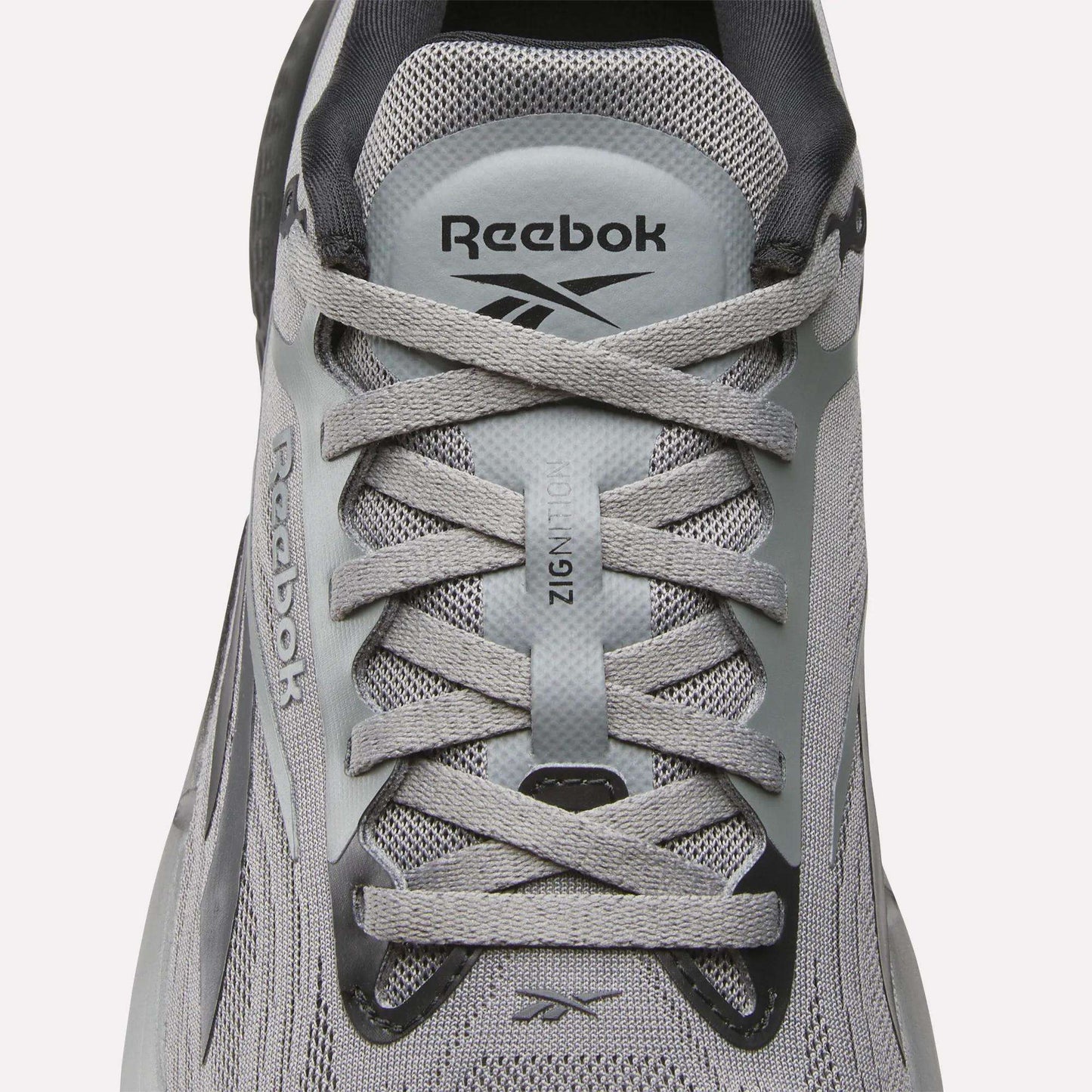 A close-up of Reebok Men's Zignition Running Shoes highlights the laces, mesh upper, and Reebok branding on the tongue and side, designed for cushioned comfort.