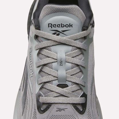 A close-up of Reebok Men's Zignition Running Shoes highlights the laces, mesh upper, and Reebok branding on the tongue and side, designed for cushioned comfort.