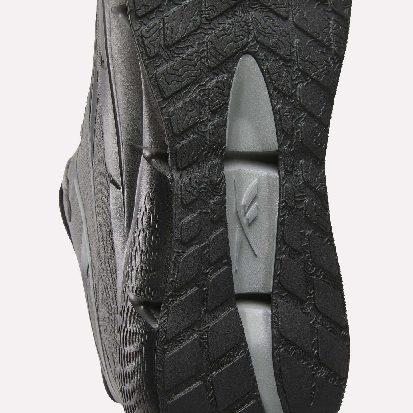 Close-up of the sole of Reebok Men's Zignition Running Shoes in black and gray, highlighting textured patterns and grooves for grip. Wavy and grid-like designs offer optimal support in these cushioned running shoes.