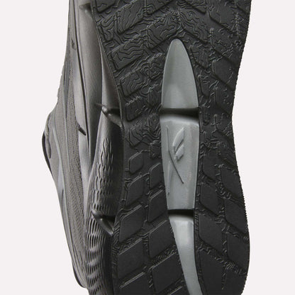 Close-up of the sole of Reebok Men's Zignition Running Shoes in black and gray, highlighting textured patterns and grooves for grip. Wavy and grid-like designs offer optimal support in these cushioned running shoes.