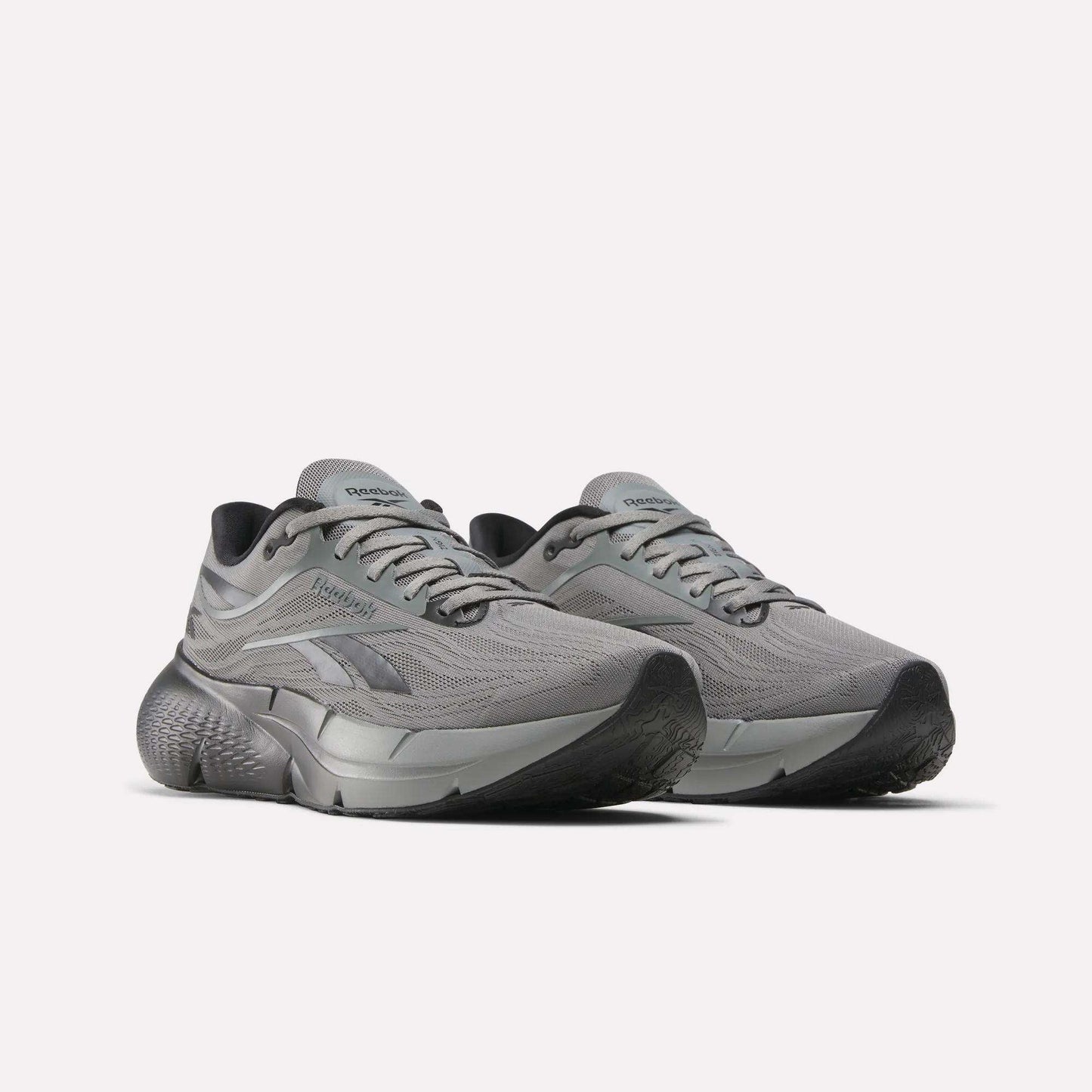 A pair of Reebok Men's Zignition Running Shoes with mesh uppers, thick textured soles, and silver accents is shown in gray on a plain white background.