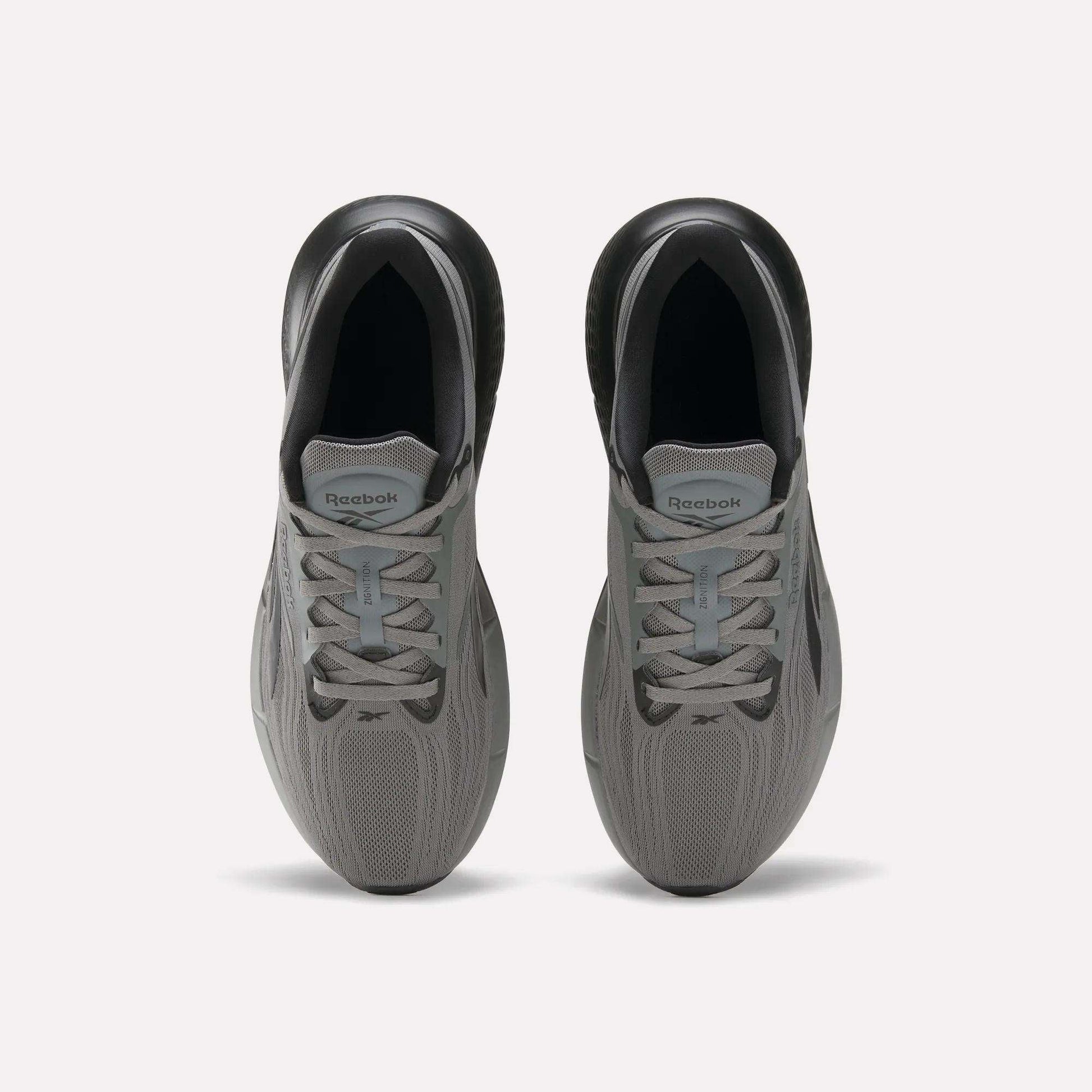 Top view of a pair of Reebok Men's Zignition Running Shoes in grey with black accents, mesh uppers, laces, and the Reebok logo on the tongue, placed side by side on a plain light background.