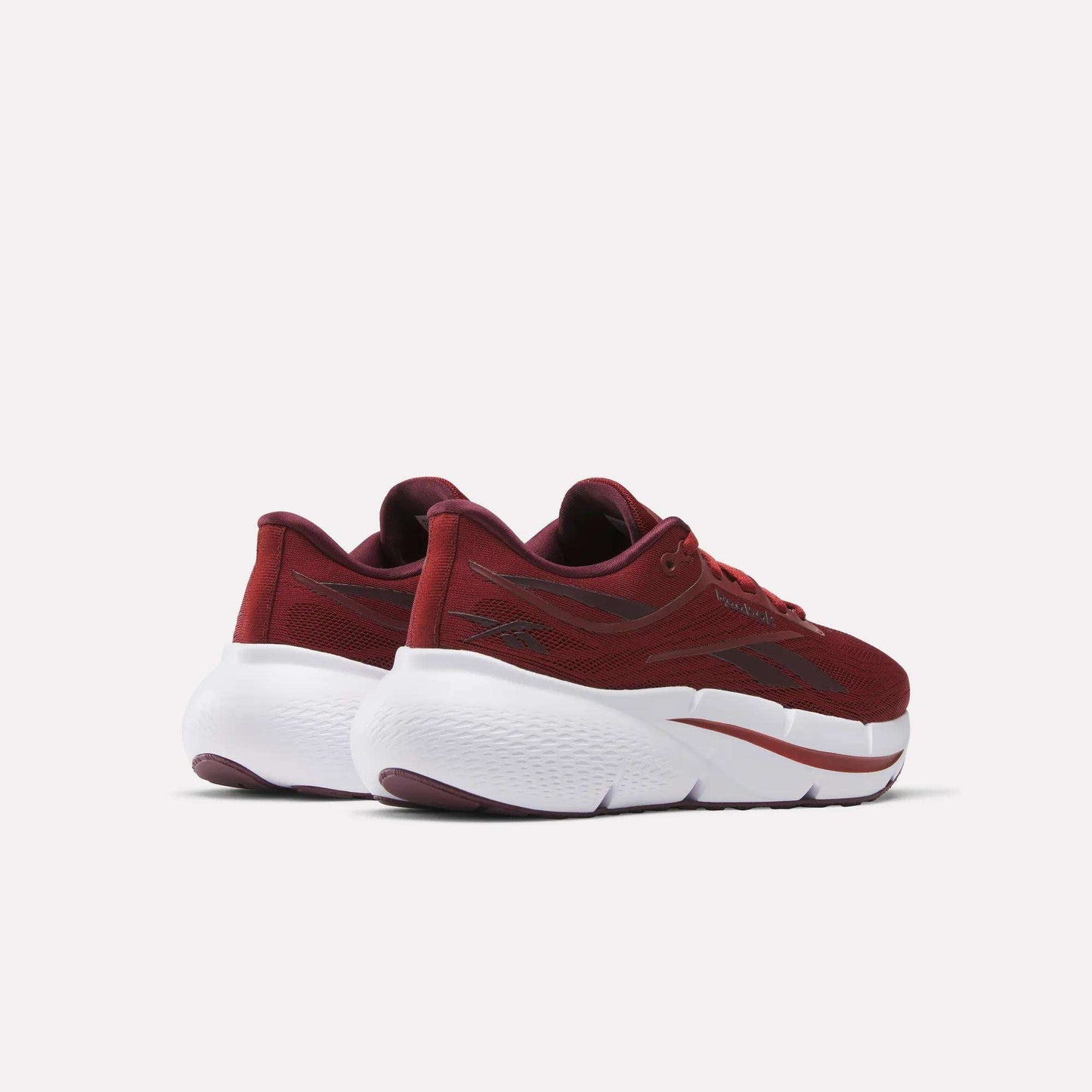 A pair of Women's Zignition Running Shoes by Reebok in maroon, featuring mesh uppers and chunky white soles, is shown from a rear side angle against a plain white background.